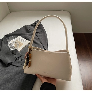 Detail of cream white faux leather shoulder bag with vintage wooden bead charm accessory