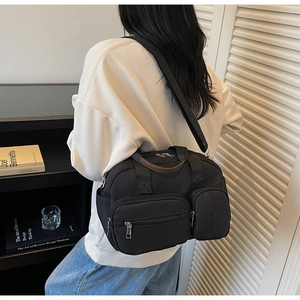 Detail of black nylon tote bag with multiple zipper pockets and brown leather handles