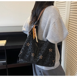 Détail du sac hobo noir mat avec motif léopard, fleurs ajourées et breloque en perles