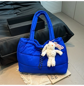 Detailed close-up of blue quilted puffer tote bag with a white plush bunny charm