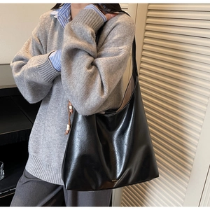 Detailed view of black oil-wax leather tote bag featuring beads charm on shoulder strap