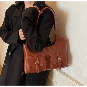 Detail of brown faux leather shoulder bag featuring dual front pockets with silver buckles