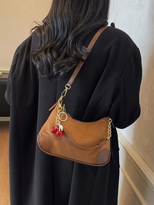 Brown suede hobo bag with cherry charm and chain strap shown on model's shoulder