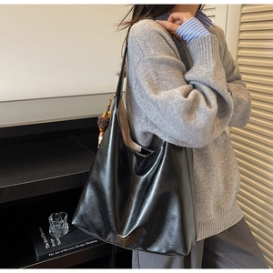 Close-up of a glossy black PU leather tote bag worn by a model in a modern office interior