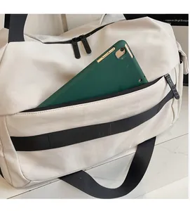 Front zipper pocket of cream travel bag showing storage space for a green tablet