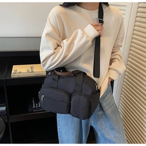 Detail of a black multi-pocket nylon crossbody bag worn with a casual outfit