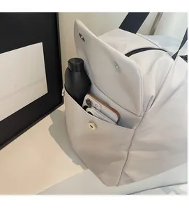 Detail view of large front pocket on beige nylon tote bag showing phone and bottle storage