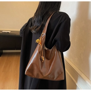 Detail of a brown leather tote bag with gold logo and vintage pompom charm decoration