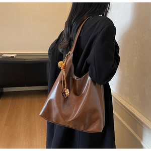 Detail shot of vintage brown leather tote bag featuring gold logo and beaded tassel