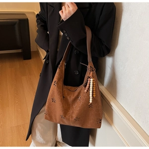 Détail du sac à bandoulière en daim marron avec motifs floraux découpés au laser et perles