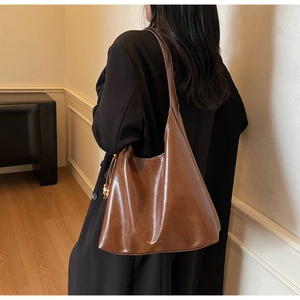 Detail view of large brown faux leather tote bag with wooden bead charm and logo