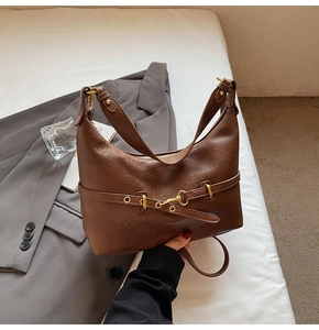 Dettaglio di una borsa a spalla in pelle marrone con cinturino vintage e fibbia dorata