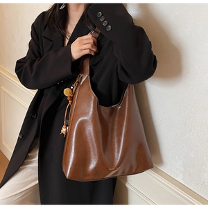 Detail of deep brown leather tote bag with gold logo lettering and decorative pompom