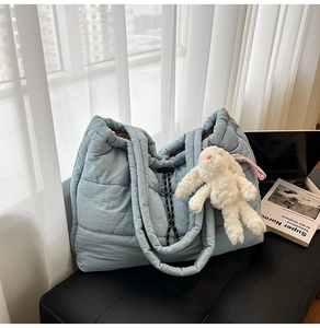 Detail of light blue quilted puffer tote bag with a cute white plush bunny charm on a stool