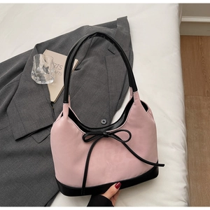 Close-up of pink suede bucket bag with black leather bow and elegant contrast trim detail