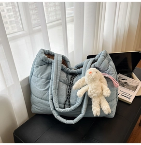 Light blue quilted puffer tote bag with white rabbit pendant on a modern black bench