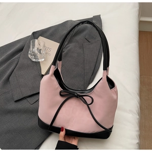 Detail of pink nylon shoulder bag with black leather bow accent and trim on white bedding