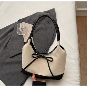 Detailed view of white tote bag with black trim and delicate bow accent on bed