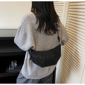 Detail view of black leopard print crescent bag with knot strap on person's shoulder