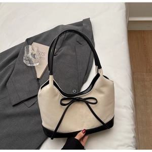 Chic beige leather shoulder bag with black trim and elegant bow detail in a lifestyle setting