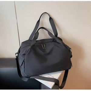 Close-up of black nylon travel bag with double zipper and strap on a leather sofa