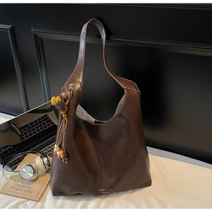 Detail view of brown leather tote bag with ethnic tassel charm and laptop in background
