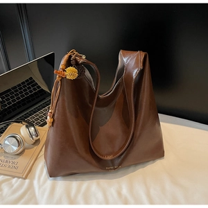 Detail of dark brown matte leather tote with floral wooden charm and gold logo detail