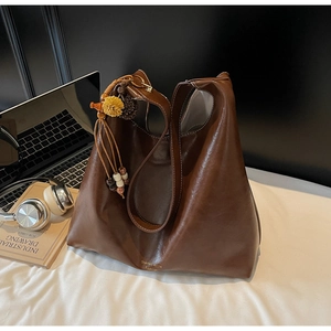 Detail of dark brown leather tote bag with ethnic tassel charm and golden lettering