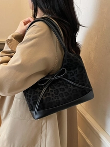 Chic black leopard print tote bag with leather bow detail on model in beige coat