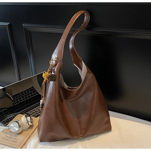 Detail view of large brown hobo bag featuring tassel charm and gold brand logo on glossy leather