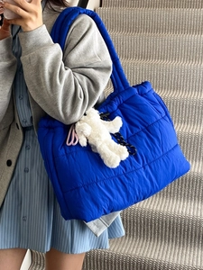 Quilted blue down tote bag with plush bear pendant shown on model in modern setting