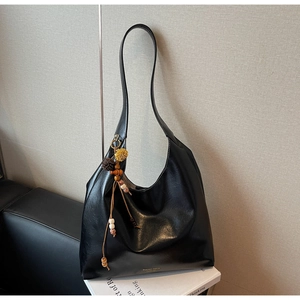 Detail of black faux leather tote with bohemian beaded tassel and gold logo lettering