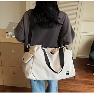 Detail view of beige nylon travel bag with black straps and side pouch on model