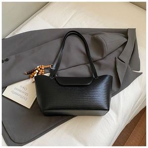 Dettaglio di borsa a spalla nera intrecciata con ciondolo di perline su blazer grigio