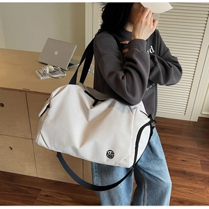 Detail view of a white large travel bag with wide black strap and side logo design