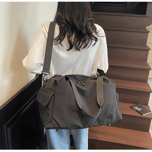 Rear view of a model carrying a large black nylon fitness bag on stairs, showing design