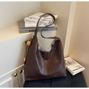 Close-up of brown leather tote bag with pompom tassel and contrast stitching detail