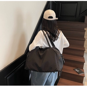 Detail of a large black waterproof nylon travel bag shown on a model in an indoor setting