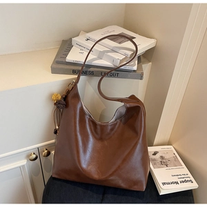 Detail view of large dark brown hobo tote bag with fringe tassel and plush pompom charm