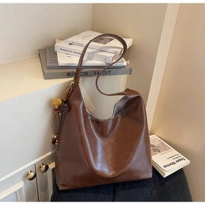 Detailed view of large dark brown hobo tote bag with a decorative tassel on a white cabinet
