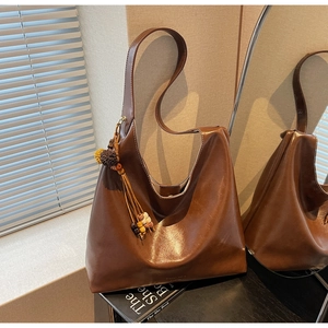 Detailed view of large brown leather tote bag with colorful tassel and bead charm