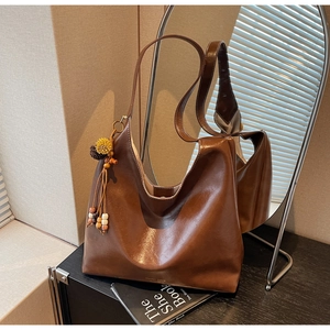 Close-up of brown soft leather tote bag with stylish wooden bead tassel and logo detail