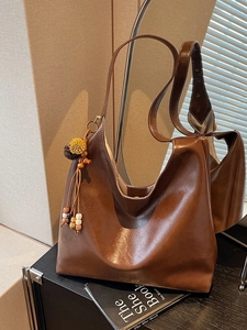 Large dark brown leather tote bag with decorative bead tassel on a mirror surface