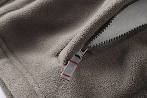 Detail of coffee grey fleece jacket featuring zippered pocket with reflective puller