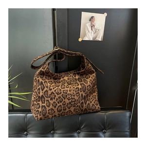 Dettaglio della borsa tote leopardata su divano in pelle nera con poster artistico