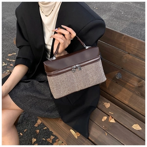 Détail d'un sac boîte en cuir marron et tissu à chevrons sur un banc de parc en extérieur