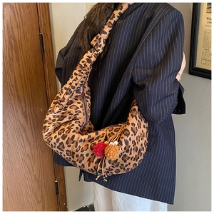 Detail of hobo bag with leopard print, wide strap, and fuzzy pompom charms on model