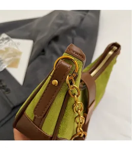 Detalle de bolso de ante verde y cuero marrón con cadena dorada y gancho metálico en D