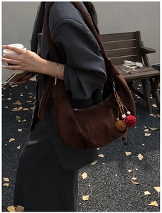 Detail of a dark brown suede hobo bag with knotted strap and tassel charm in autumn street setting
