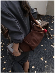 Detail of a dark brown suede crescent shoulder bag with a red pompom and leather tassel